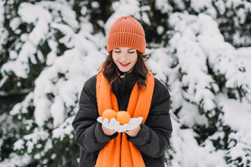 Woman in orange winter attire holding a tangerine, smiling playfully in snow-covered surroundings. Winter wellness, mindfulness, and seasonal joy.
