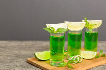 Sweet refreshing mint liqueur, with ice and mint leaves on table background, Shots with lime slice and mint flat lay