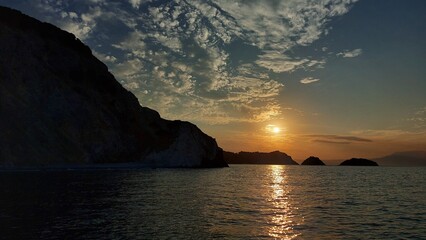 Beautiful sunset going down in the sea water behind mountains.