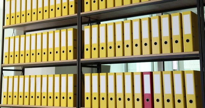 Red business folder is quickly moving among yellow ones on shelf in office. Storage of business documents