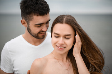 Obraz premium The man hugs the bride from behind by the shoulders and looks at her face, which she turned to him