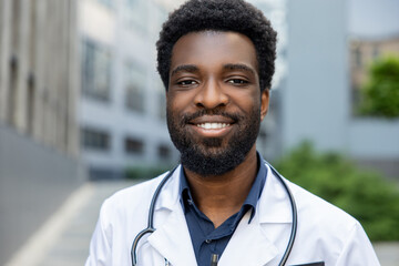 Cheerful man doctor in uniform looking at camera standing outdoor medical center