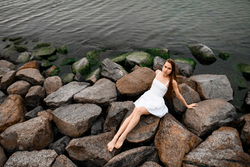 Top view of a beautiful young woman sitting on a stone resting her hands on the stones and looking at the camera