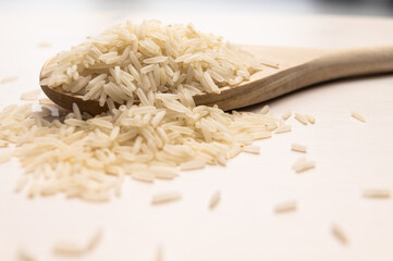 Raw basmati rice, in wooden ladle, on light wooden surface.