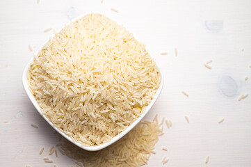 Raw basmati rice, in white bowl, on light wooden surface.