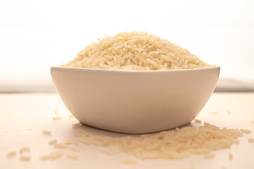 Raw basmati rice, in white bowl, on light wooden surface.