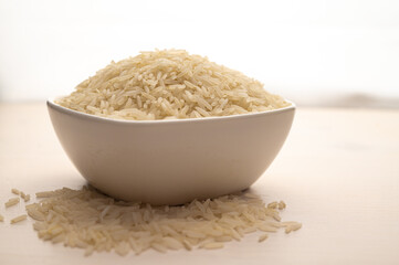 Raw basmati rice, in white bowl, on light wooden surface.