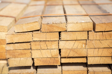 Stacked wooden planks in a lumberyard, showing various shades and textures of the wood, arranged in neat rows..