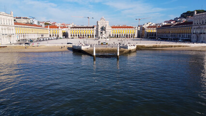 Fototapeta premium Uma imagem icónica do Terreiro do Paço (também conhecido como Praça do Comércio), situada na Baixa Pombalina, em Lisboa. A ampla praça está rodeada por majestosos edifícios de cor amarela com arcadas 
