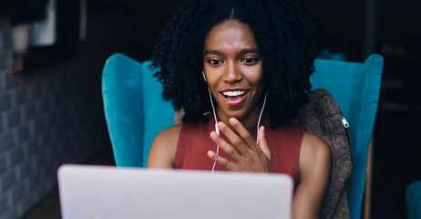 Happy dark skinned hipster girl feeling surprised from motivated information received from online webinar, shocked excited from high speed internet connection for downloading music playlist on netbook