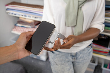 Unknown woman owner processes transaction with credit card reader in the fabric shop