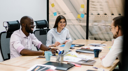Happy male and female colleagues communicated in modern office during break of conference, successful partners sitting at desk and discussing ideas for project while cooperating togetherness