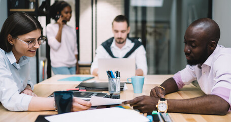 Multicultural people dressed in formal wear discussing productive strategy of design project during briefing in modern office, intelligent male and female colleagues collaborating on working plan