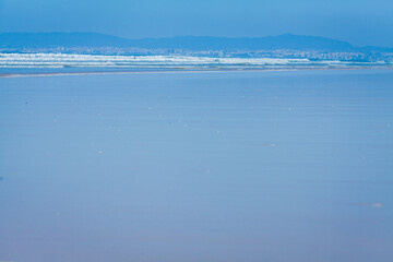 This image presents a serene coastal view featuring a long, reflective stretch of shallow water on the beach.