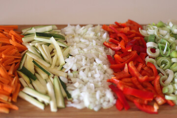 Chopped leek, red pepper, onion, zucchini and carrot on the chopping board. Cooking and meal prepping at home. Selective focus.