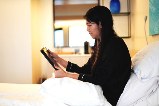 Young asian business woman working on a business trip video calling her colleague and working with tablet while relaxing on bed in a luxury hotel room and this is a travel and business concept. - Powered by Adobe