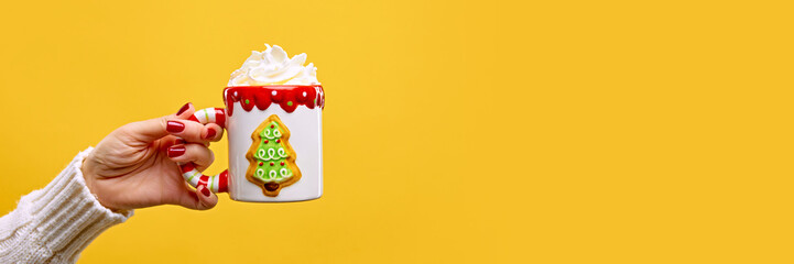 Female hand holding funny but cozy cup of Irish Coffee topped with whipped cream against warm yellow studio background. Concept of festive winter drink, cafe and catering, Christmas mood. Ad