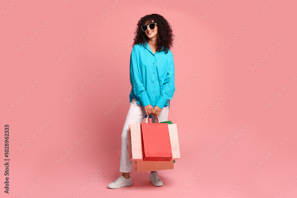 Wall mural smiling woman with colorful shopping bags on pink background