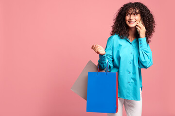 Smiling woman with colorful shopping bags talking by smartphone on pink background. Space for text