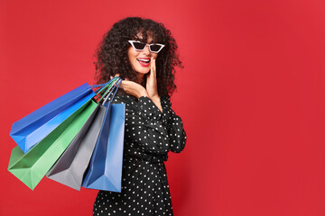 Happy woman with colorful shopping bags on red background. Space for text