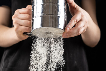 The cook sifts the wheat flour through a metal sieve
