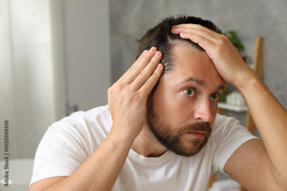 Wall mural man with hair loss problem looking at mirror indoors