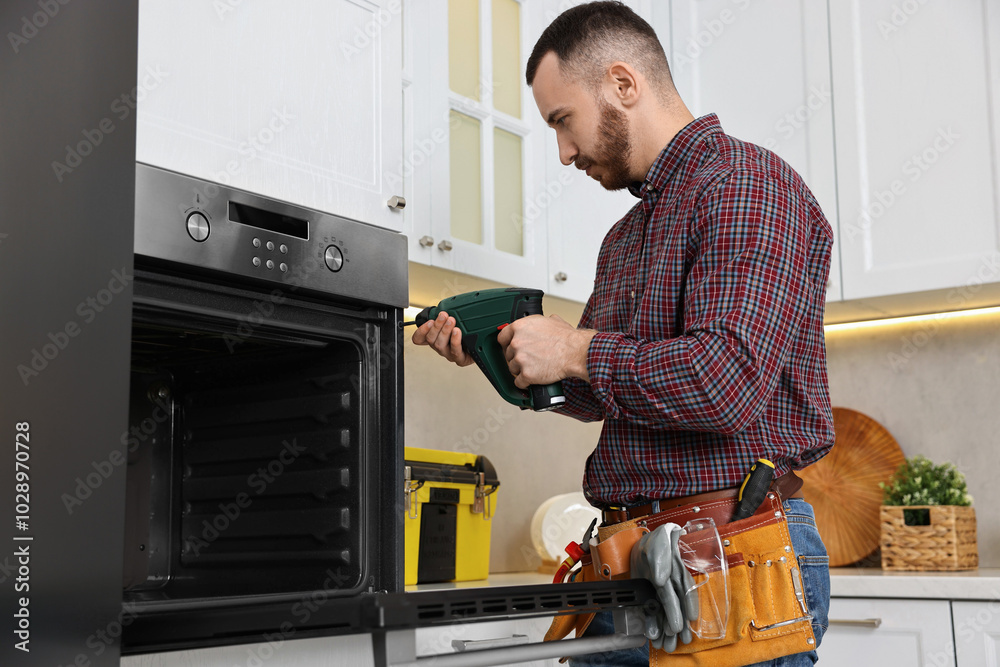 Poster Repairman with electric screwdriver fixing oven in kitchen