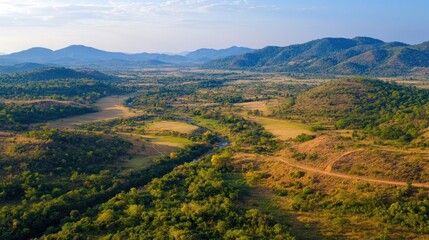 Obraz premium Aerial view of a valley with rolling hills, green fields, and a winding river.