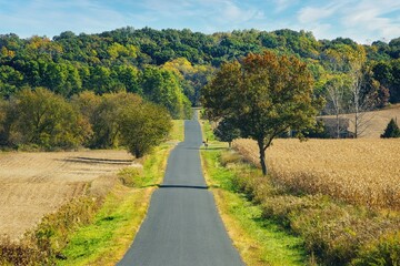 Autumn landscape of a hilly rural road passing by fields and entering a distant forest in the countryside near Galesville, Wisconsin, USA.