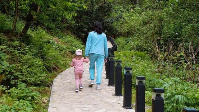 Mom and daughter walk along a path in the park. Mountain landscape. Lots of greenery