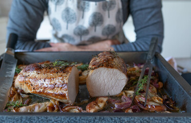 Homemade oven roasted pork loin served by a woman with apron in the kitchen
