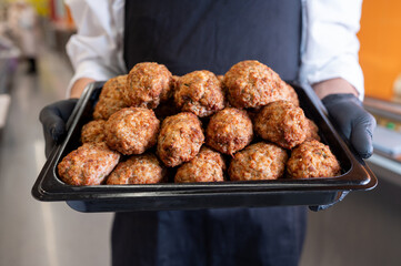 The cook's hands in black gloves hold a tray of fried cutlets in a supermarket, his own production. An environmentally friendly product. Meat dishes