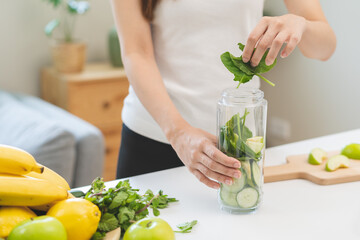 Vegetable smoothie detox, woman hand making healthy raw fresh green fruit juice with blender machine, preparing drink with spinach in kitchen at home, eating vegan diet. Healthy dieting, weight loss.
