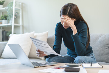 Stressed asian young employee, business woman calculate tax, income and expenses, hand holding bills of credit card for payment or payday on table at home office. Financial, finance people concept.