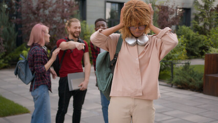 Fototapeta premium Group of angry students teenagers multiracial classmates mock humiliate bully mockery at college university outdoors discriminate thumbs down African American sad woman student stressed girl problem