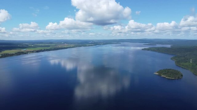 Panoramic aerial drone view of Lake Matapedia showcasing villages, cultivated fields, surrounding mountains and drifting clouds across the Matapedia Valley in Quebec, Canada.