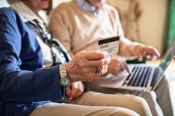 Happy senior couple online shopping on laptop from home couch
