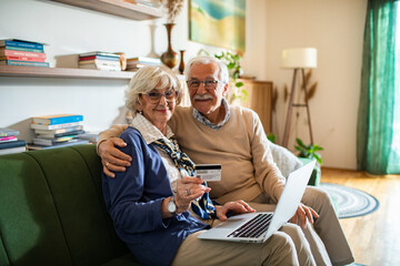 Happy senior couple online shopping on laptop from home couch