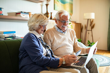 Happy senior couple online shopping on laptop from home couch