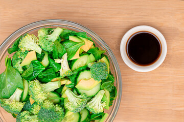 Fresh Green Salad of Avocado, Broccoli, Spinach and Cucumber for Detox with Soy Sauce on Wooden Cutting Board. Vegan Salad. Vegetarian Culture. Raw Food. Healthy Eating and Vegetable Diet