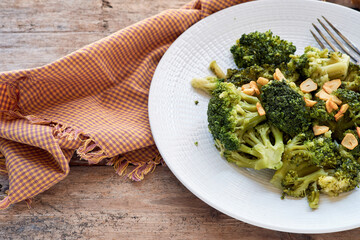 Sautéed broccoli with garlic on a white plate next to a checkered tablecloth on a rustic wooden table