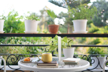 Laptop side view and yellow coffee cup with notebooks on white metal table outdoor balcony