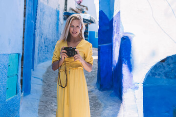 Portrait of woman with retro camera enjoying free day in Chaouen historic center, positive female photographer exploring Morocco during vacations using vintage equipment for recreating with hobby