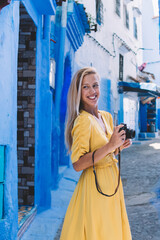 Joyful woman with retro camera enjoying free day in Chaouen historic center, excited female photographer exploring Morocco during vacations using vintage equipment for recreating with hobby