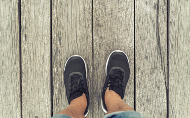 Male legs in black sneakers against the background of a road made of old wooden planks.