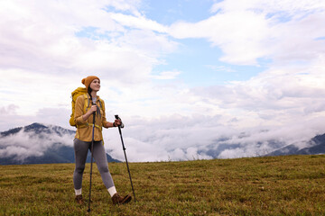 Young hiker with trekking poles and backpack in mountains outdoors, space for text