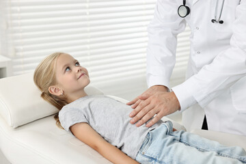 Doctor examining little girl with stomach pain in hospital, closeup
