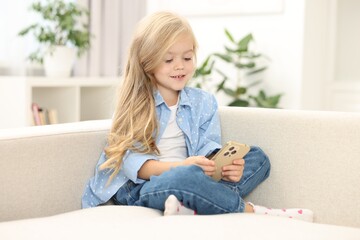 Cute little girl using smartphone on sofa at home