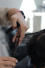 Naklejka premium close up of a hairdresser's hands cutting a young man's hair.