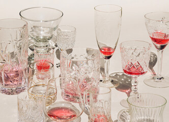 Wine glasses with red and pink drinks and shadows on sunny day. Cocktails crystal glasses on beige background.